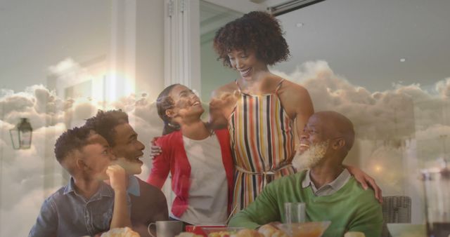 Mixed-race family smiling and enjoying breakfast together in a cozy home setting. Ideal for use in advertising family-related products, concepts of togetherness, or breakfast food promotions. The warm and joyful atmosphere makes it suitable for marketing campaigns focused on family values, intergenerational connections, and diverse representation.