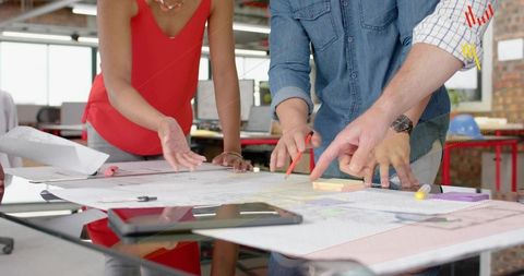 Architectural team collaborating over plans pointing tracing using tablet in modern studio
