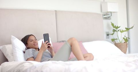 Teen Girl Relaxing on Bed Using Smartphone in Cozy Room