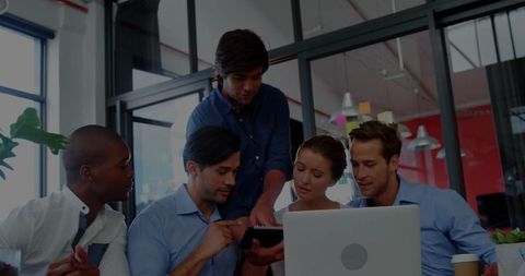 Team collaborating around laptop and tablet in modern open-plan office with coffee