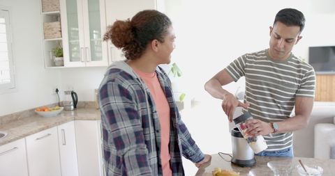 Smiling gay couple making fruit smoothie in kitchen