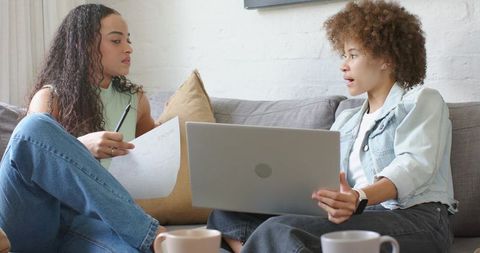 Two African American Women Collaborating on Laptop and Documents While Discussing Plans