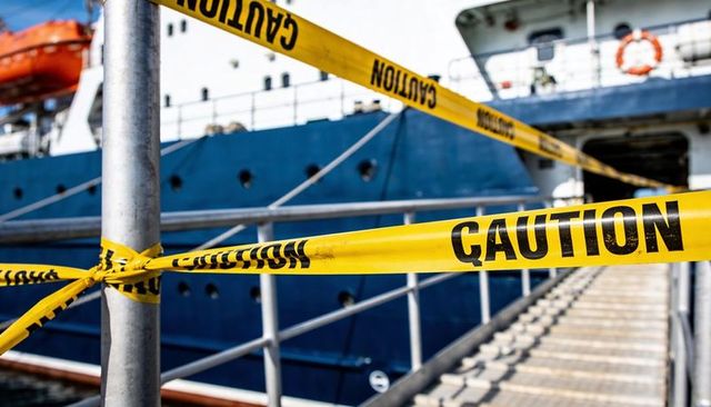 Yellow caution tape blocking gangway to docked vessel at harbor pier for safety and repair
