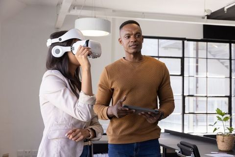 Diverse coworkers testing VR headset while collaborating with tablet in open-plan office