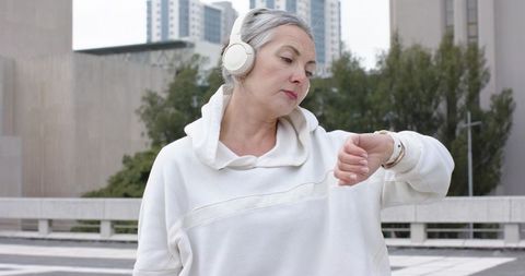 Mature woman checking smartwatch while wearing headphones on urban rooftop plaza