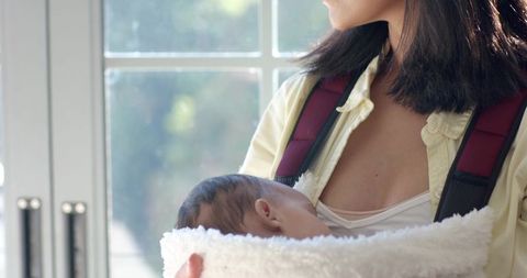 Asian mother gently cradling infant by sunlit window