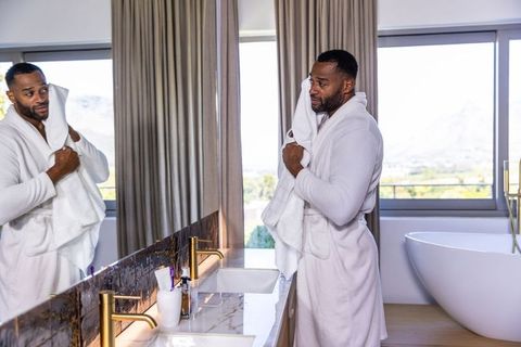 Mature african man drying face at luxury marble vanity wearing white robe and holding towel