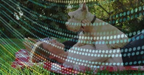 Relaxing woman holding terrier on picnic blanket in sunny park with dotted light overlay