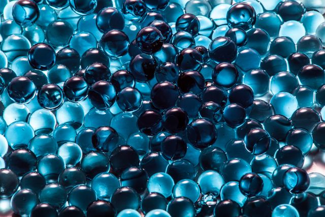 Blue transparent gel beads clustered together creating a shiny and reflective surface. Perfect for backgrounds, abstract art projects, texture references, and designs emphasizing hydration, freshness, or cooling effects.