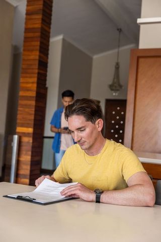 Male colleagues reading documents and checking phone in modern lobby with wood column