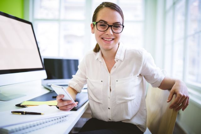 Portrait of smiling female graphic designer sitting at desk in creative office