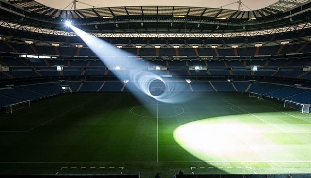 Spotlight forming spiral vortex over empty soccer stadium illuminating center circle under roof
