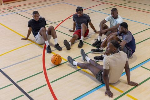 African american men sitting stretching and talking on indoor basketball court team camaraderie