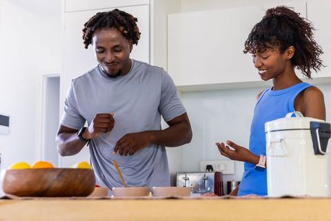 African american couple cooking and stirring meal in modern sunlit kitchen wearing smartwatches