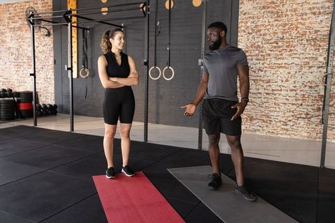 Diverse male trainer coaching female client on exercise mats by pull-up rig with rings