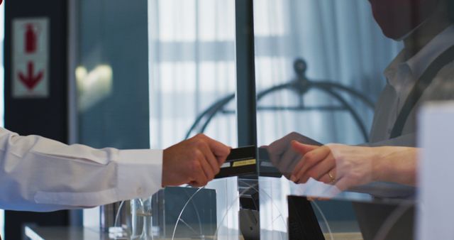 Hand giving credit card to receptionist at hotel front desk. Useful for illustrating booking reservations, customer service in the hospitality industry, or payment transactions in hotels. Also suitable for articles or advertisements about traveling, lodging experiences, and hotel check-in processes.