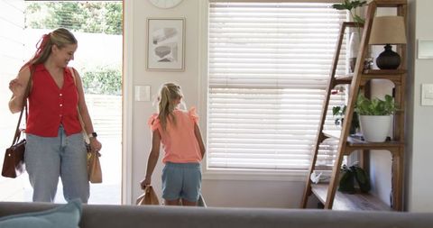 Mother and daughter arriving home carrying grocery bags in bright sunlit entryway