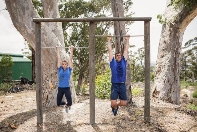 Fit man and woman performing pull-ups on bar during obstacle course in boot camp