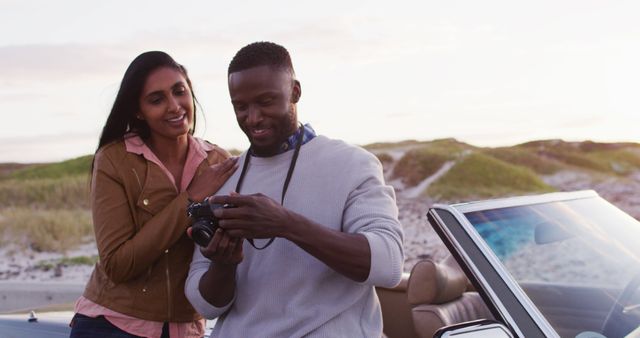 African american couple using digital camera to take pictures while standing near the convertible car on the road. road trip travel and adventure concept