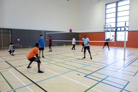 High school indoor volleyball team practicing on gym court with players serving and diving