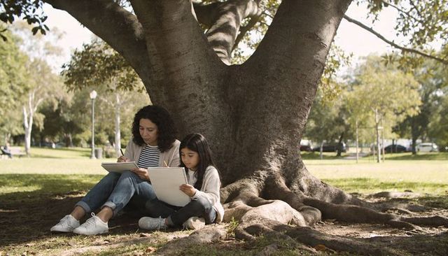 Mother and daughter sketching together on tree roots in sunlit park with calm mood