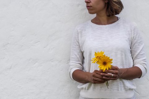 Woman holding sunflowers against white wall