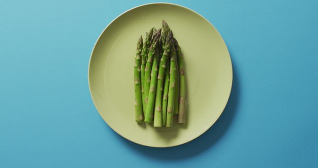 Photo showing fresh asparagus spears arranged on green plate, placed against a blue background. Can be used for promoting healthy eating, vegetarian recipes, organic food, cooking blogs, or dietary plans.