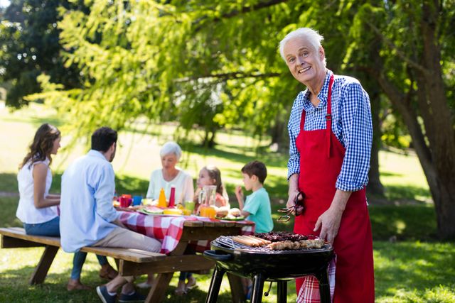 Portrait of senior man barbequing with family in background