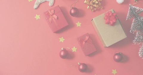 Festive flat lay featuring kraft gift box with red bow, red baubles and gold star confetti