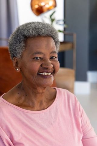 Senior african american woman smiling wearing pink top and pearl earrings in cozy living room