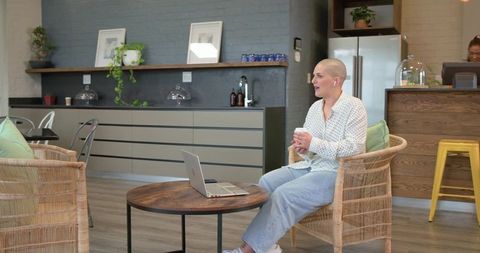 Freelancer working remotely in cozy cafe on wicker chair with laptop and takeaway coffee