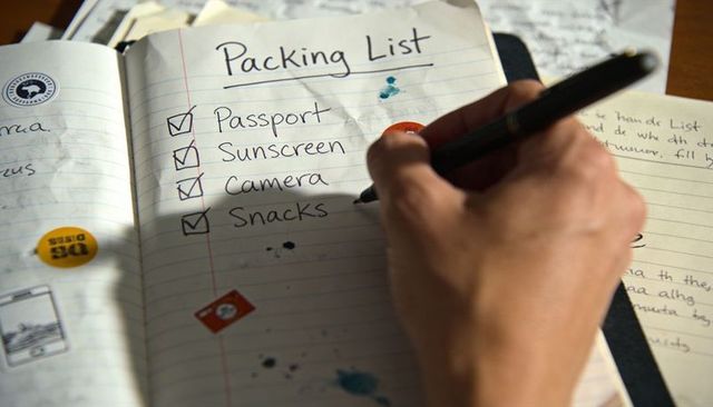 Handwritten packing list with checked passport, camera, sunscreen, snacks for travel planning