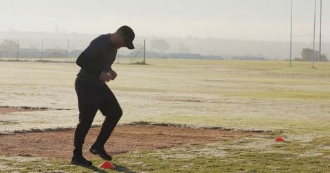 Mature athlete performing agility drills at dawn on dew-covered field with cones