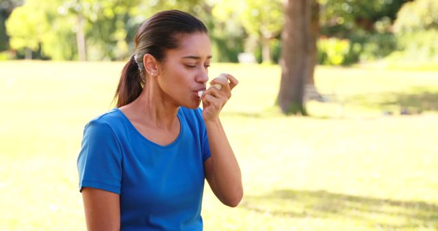 Young woman seated in a park using an asthma inhaler on a sunny day, providing relief for her respiratory condition. Ideal for content related to respiratory health, asthma management, outdoor healthcare, and allergy treatment. Can be used in medical blogs, health websites, and asthma awareness campaigns.