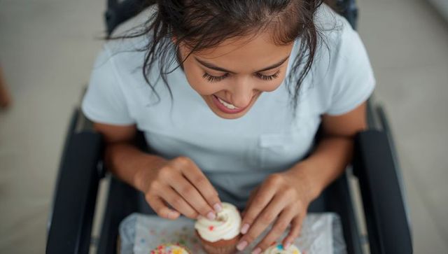 Smiling woman in wheelchair decorating cupcakes at home, inclusive baking and accessibility