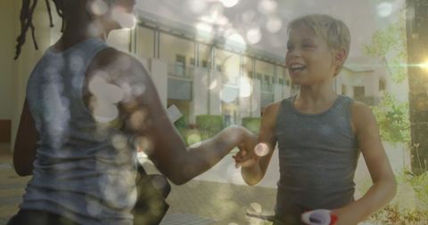 Joyful schoolboys shaking hands outdoors under sunshine