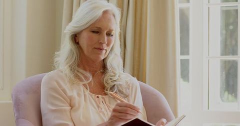 Senior Woman Writing Thoughts in Journal by Sunny Window