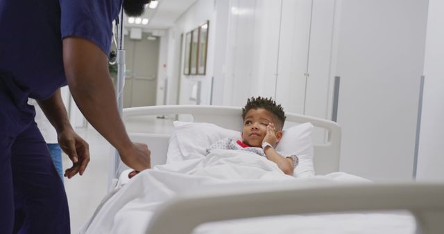 African american male doctor talking to child patient laying in bed at hospital. Medicine, healthcare, lifestyle and hospital concept.