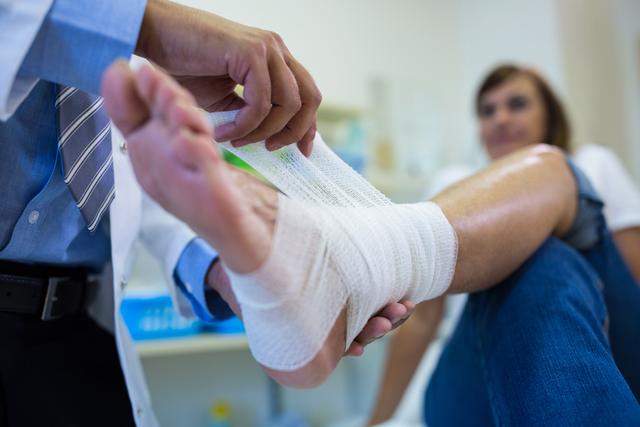 Doctor bandaging female patient's foot in hospital. Ideal for use in healthcare, medical care, injury treatment, and hospital-related content. Can be used in articles, blogs, and educational materials about medical care and patient treatment.