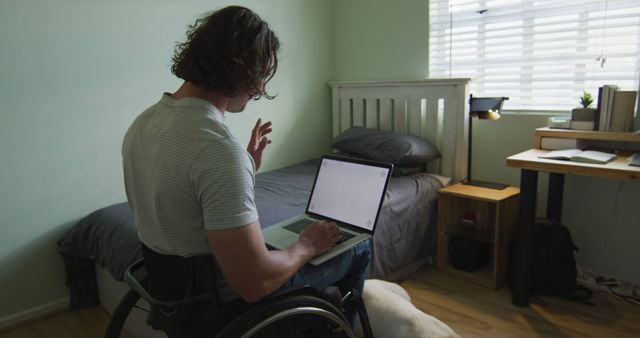 Man in wheelchair working on laptop in minimalist bedroom - Download Free Stock Images Pikwizard.com