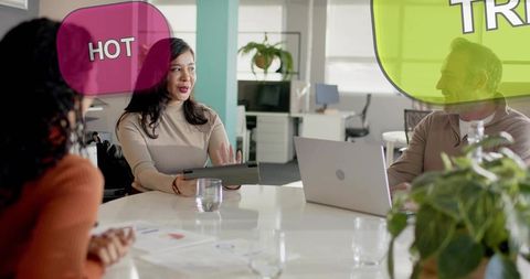 Leading woman presenting with tablet and laptop in modern open-plan office meeting