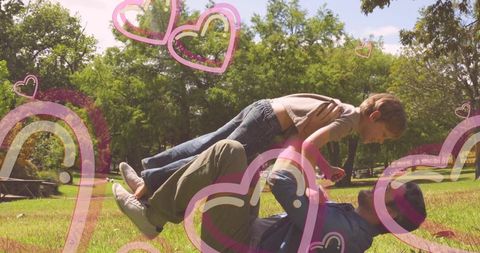 Father and son playing airplane on grass with heart and rainbow graphic overlays
