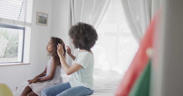 Biracial mother and daughter brushing hair with hairbrush. Family, motherhood, childhood, hygene and togetherness, unaltered.