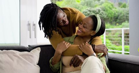 Couple Embracing on Sofa Showing Smartwatch in Sunlit Balcony Interior Cozy Romance Moment