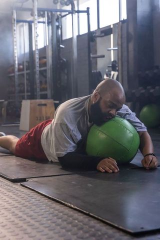 Exhausted athlete resting on green medicine ball after intense workout in industrial gym