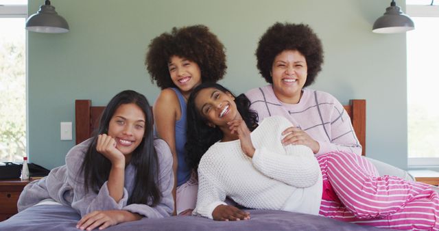 Portrait of happy diverse female friends lying on bed and smiling in bedroom. spending quality time at home.