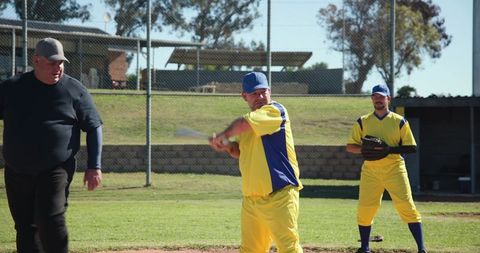 Amateur baseball team playing on sunny field with batter swinging and teammate ready