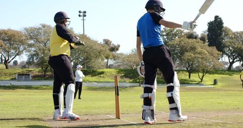 Cricketers Preparing to Bat on Grass Field under Bright Sky