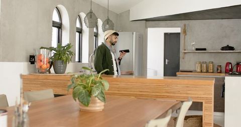 Indian man checking smartphone in modern minimalist open-plan kitchen with wooden island