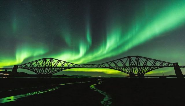 Northern lights illuminating steel cantilever bridge over tidal estuary